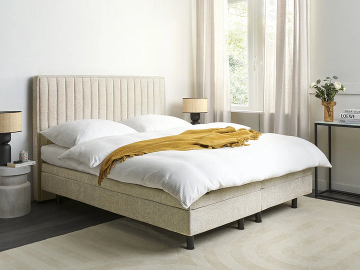 Beige upholstered bed with white bedding and a yellow blanket in a bedroom setting.