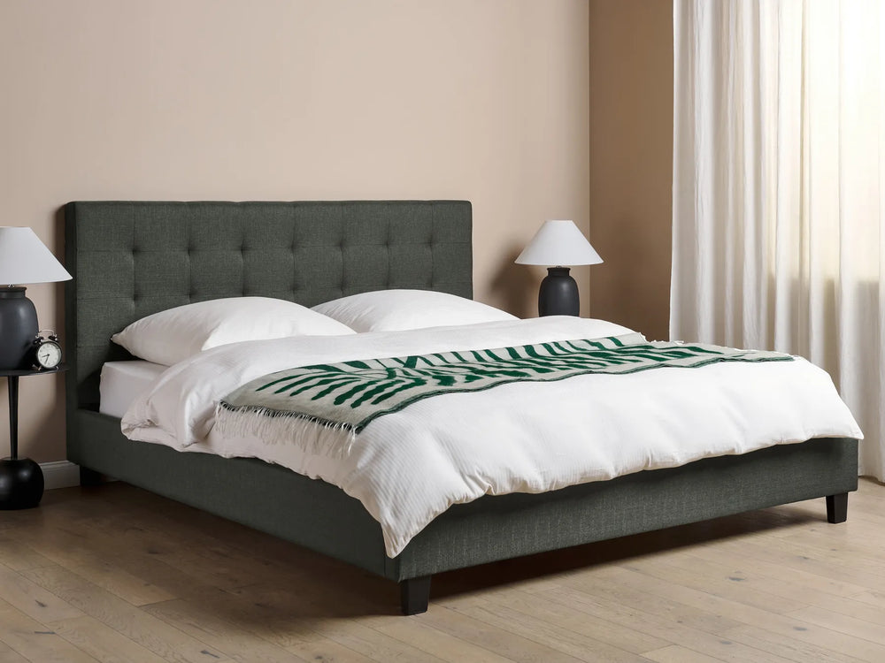 Gray upholstered bed with white bedding and a green patterned throw in a bedroom setting.