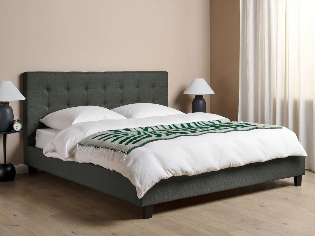 Gray upholstered bed with white bedding and a green patterned throw in a bedroom setting.