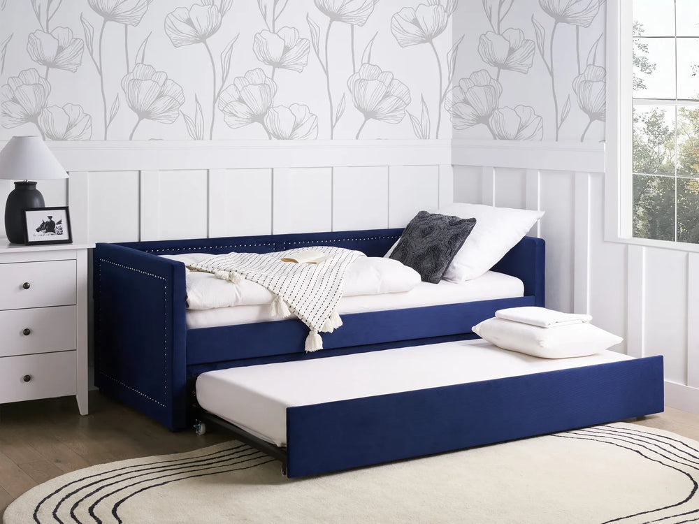 Blue sofa bed with white bedding in a room with floral wallpaper and a window.