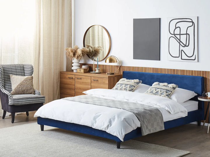 Modern bedroom with a blue bed, armchair, and wooden dresser.