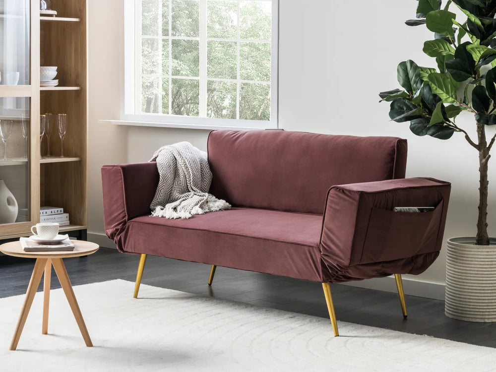Maroon sofa with gold legs in a living room setting with a plant and small table.