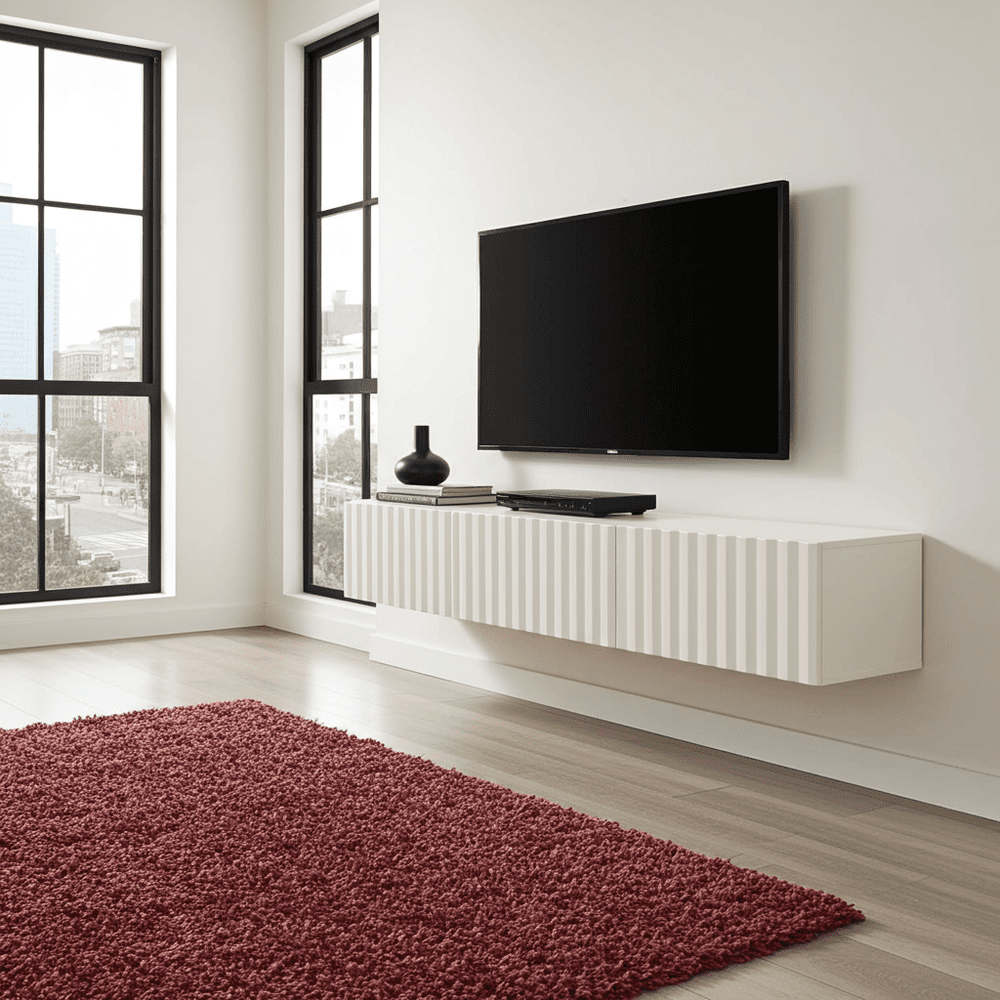 Modern living room with a flat-screen TV on a white wall, red rug, and large windows.