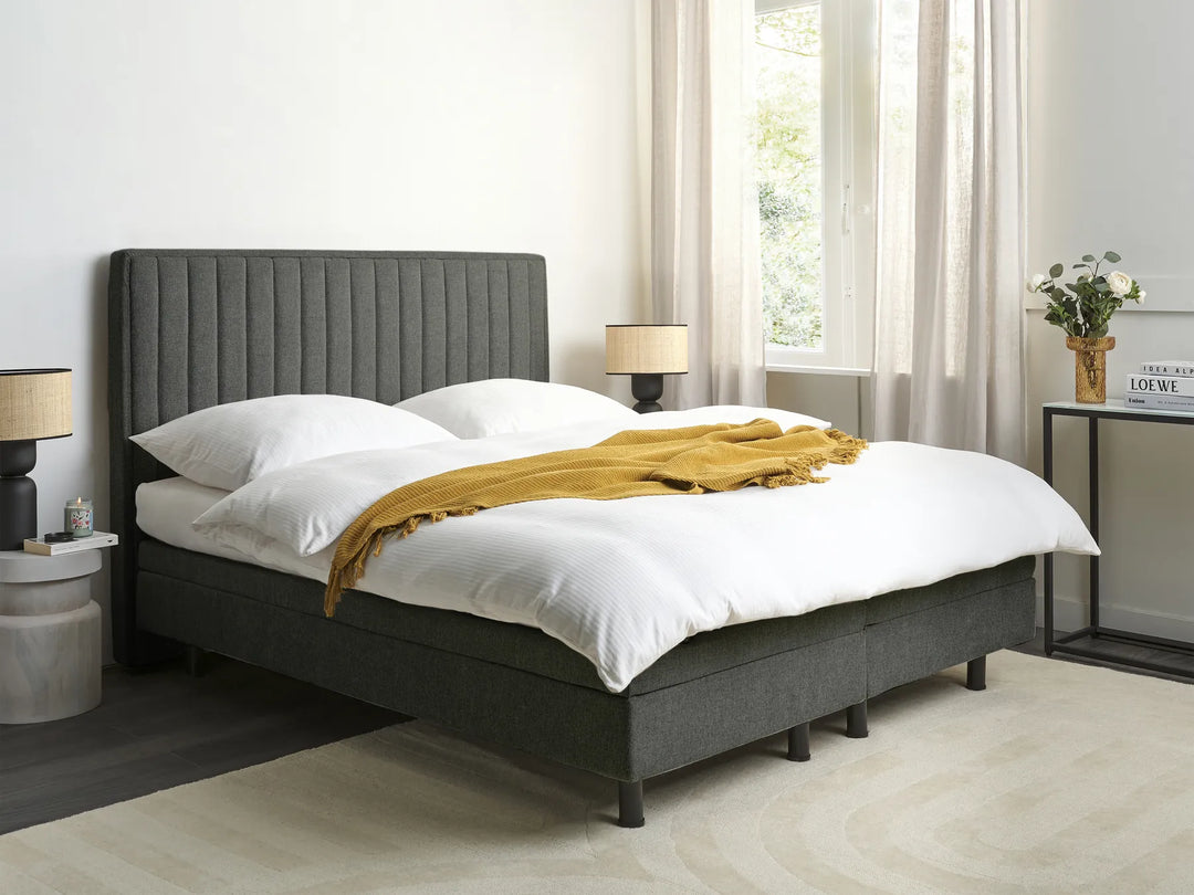 Gray upholstered bed with white bedding and a yellow blanket in a bright bedroom.