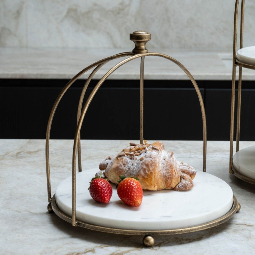 Decorative metal stand with a croissant and strawberries on a marble surface