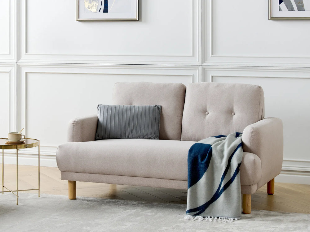 Beige sofa with a gray pillow and blue blanket in a living room setting.