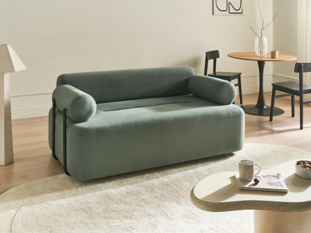 Green sofa in a living room setting with a table and chairs.
