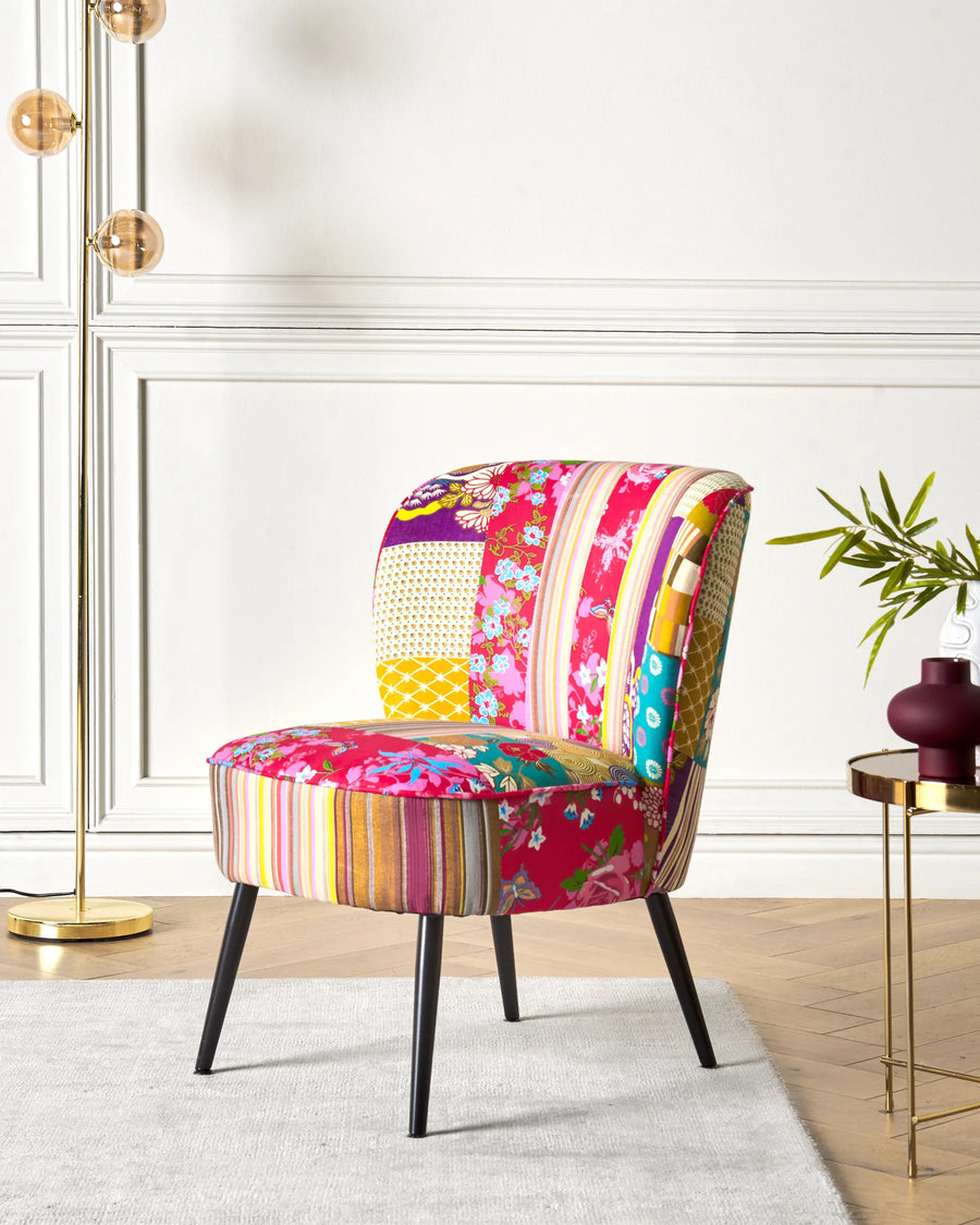 Colorful patchwork chair in a modern interior setting with a plant and side table.
