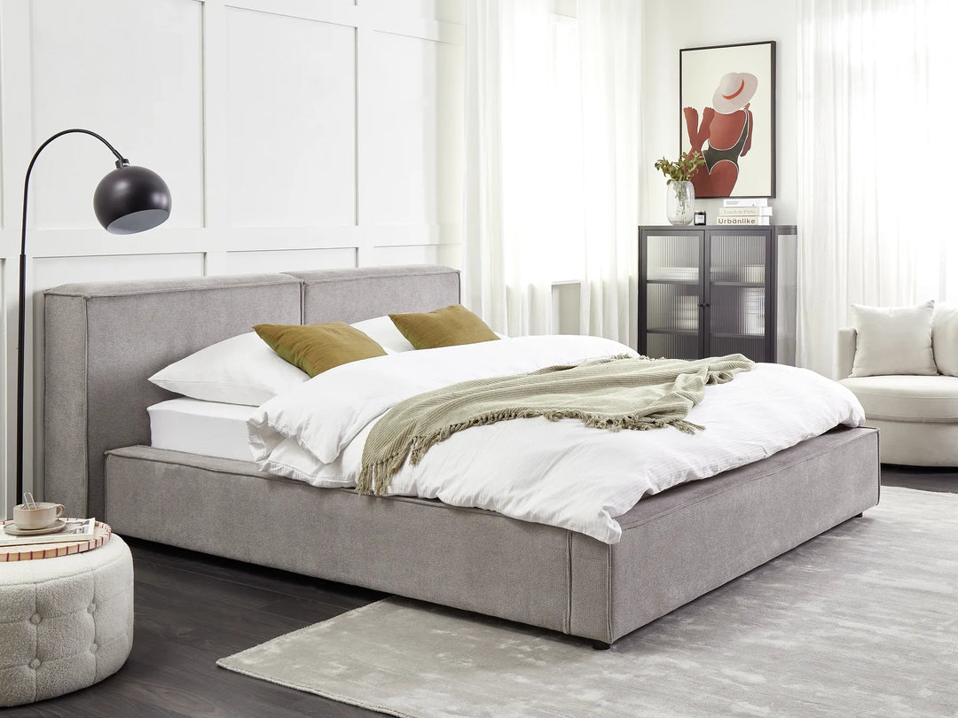 Gray upholstered bed in a modern bedroom with white walls and decor.