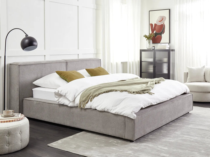Gray upholstered bed in a modern bedroom with white walls and decor.