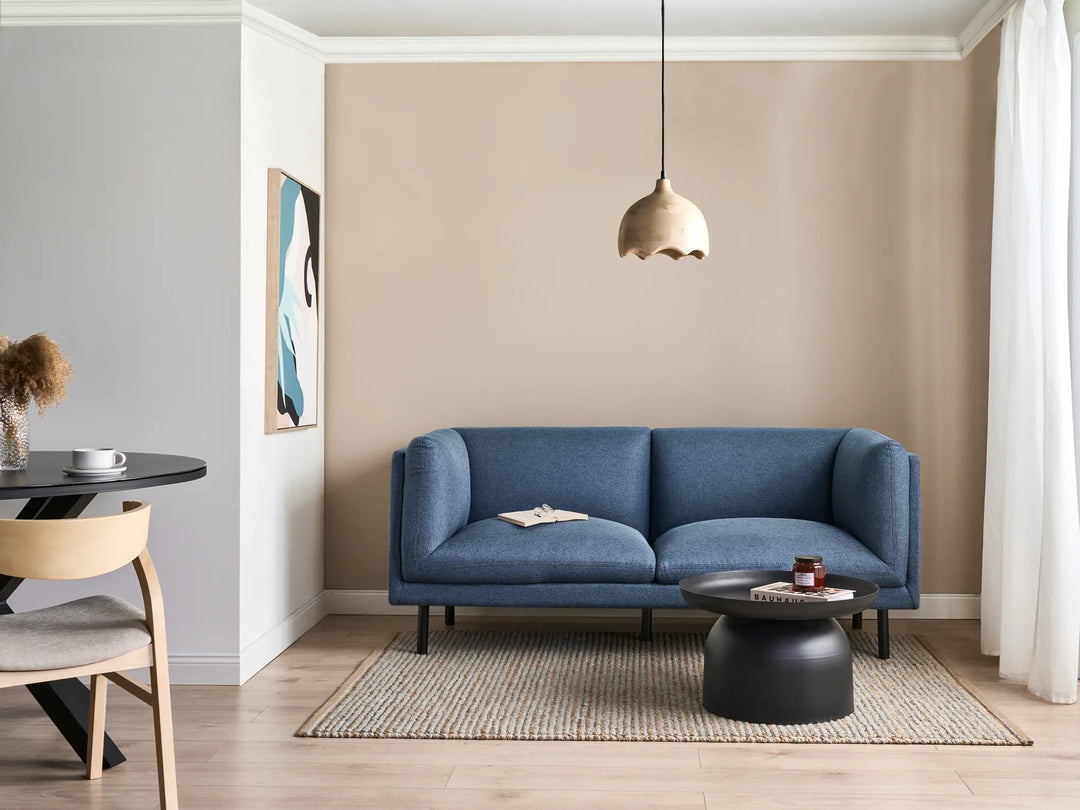 Modern living room with a blue sofa, round black coffee table, and pendant light.