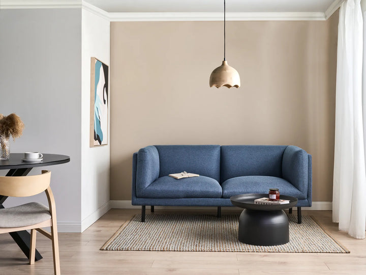 Modern living room with a blue sofa, round black coffee table, and pendant light.