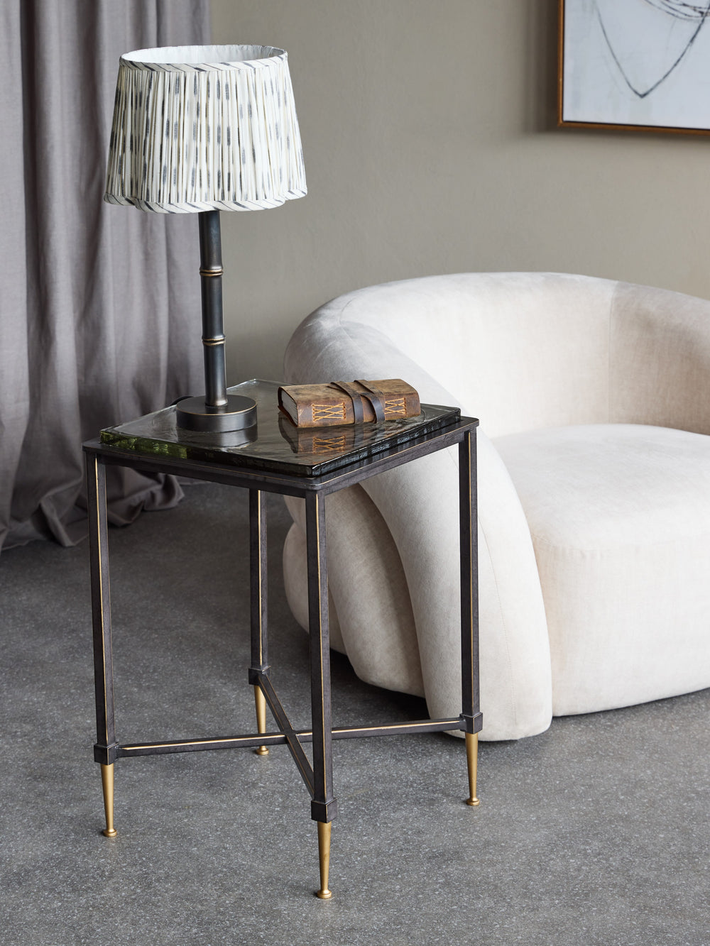 Small side table with a lamp and decorative items next to a white armchair in a room.