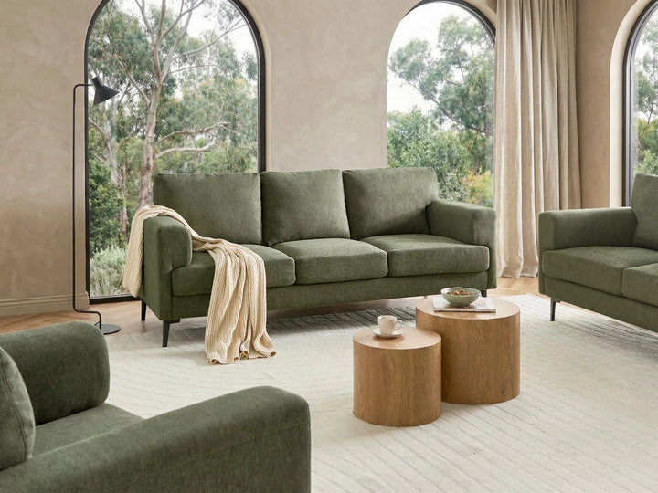 Green sofa in a modern living room with wooden coffee tables and large windows.
