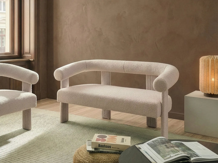 Beige armchair in a room with a lamp and books on a rug