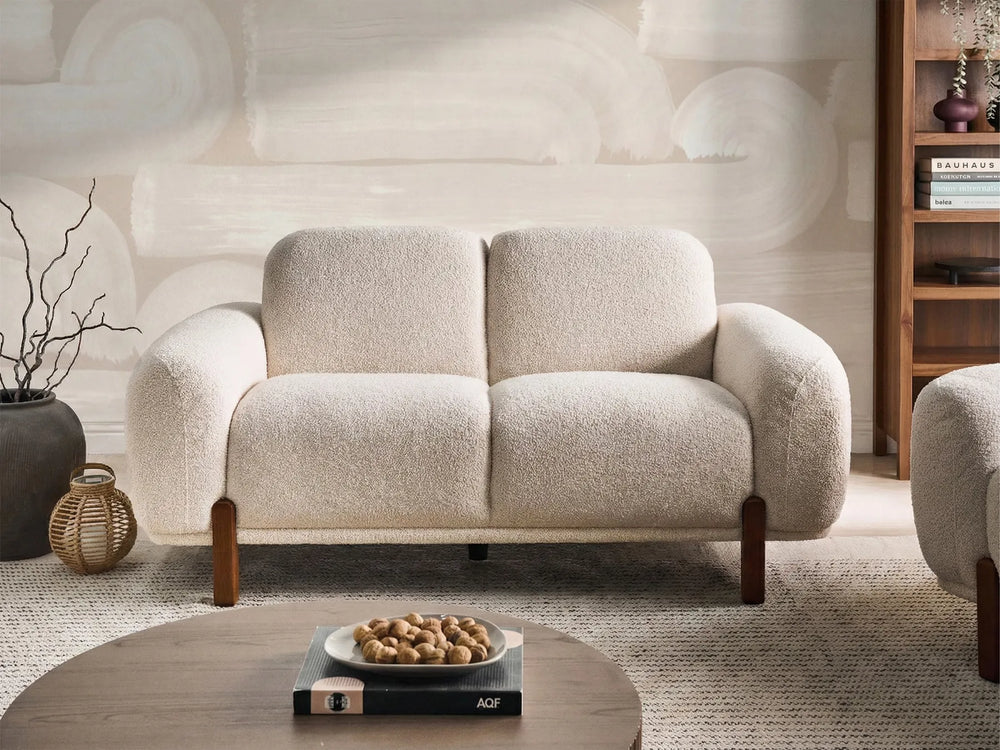 Beige sofa in a room with a textured wall and wooden shelf.