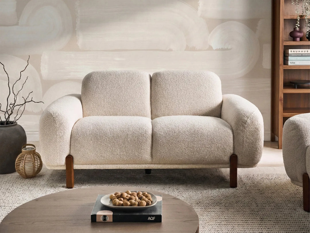 Beige sofa in a room with a textured wall and wooden shelf.