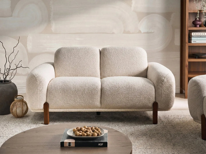 Beige sofa in a room with a textured wall and wooden shelf.
