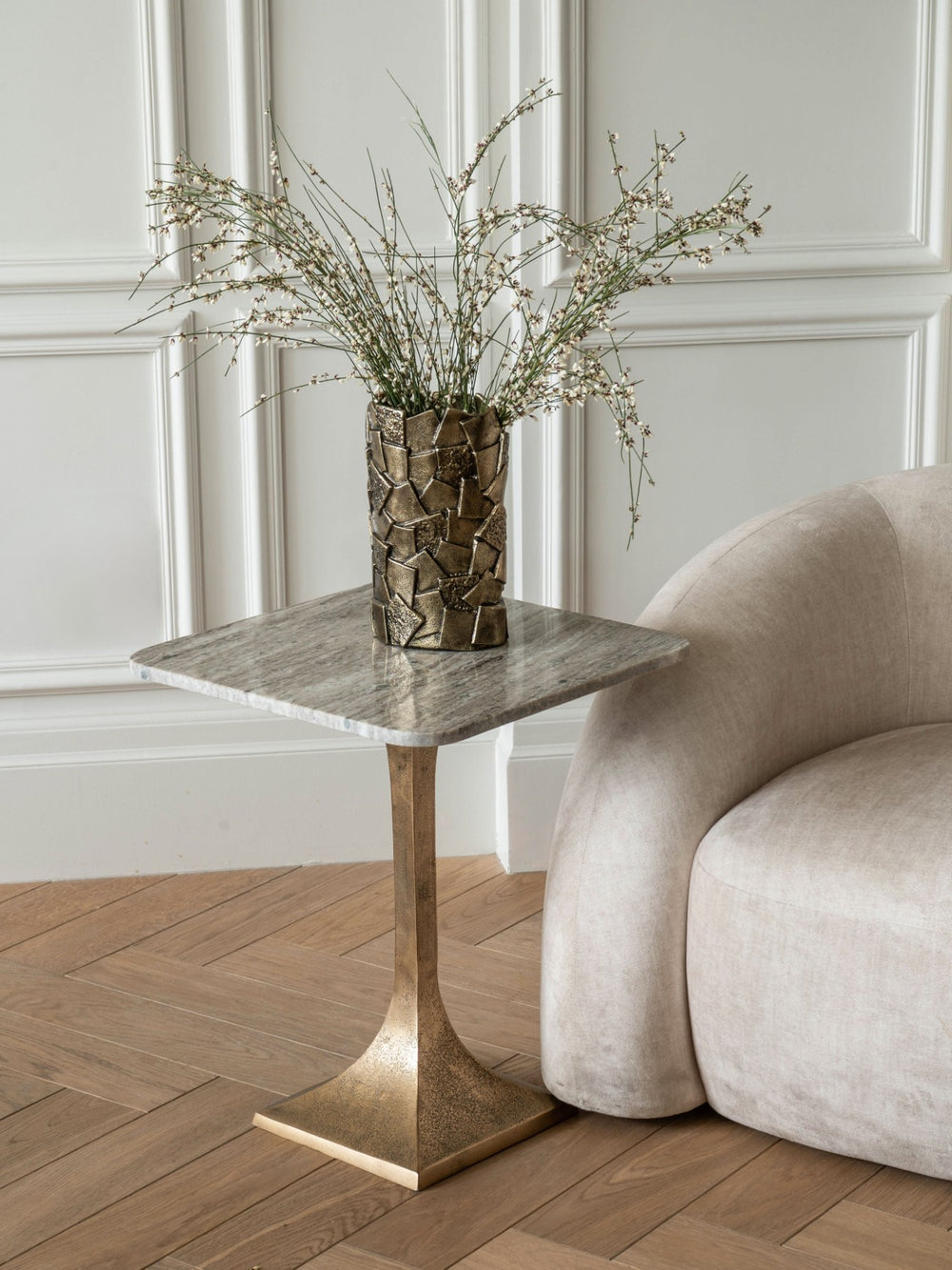 Side table with marble top and bronze base next to a beige sofa in a room with panelled walls.