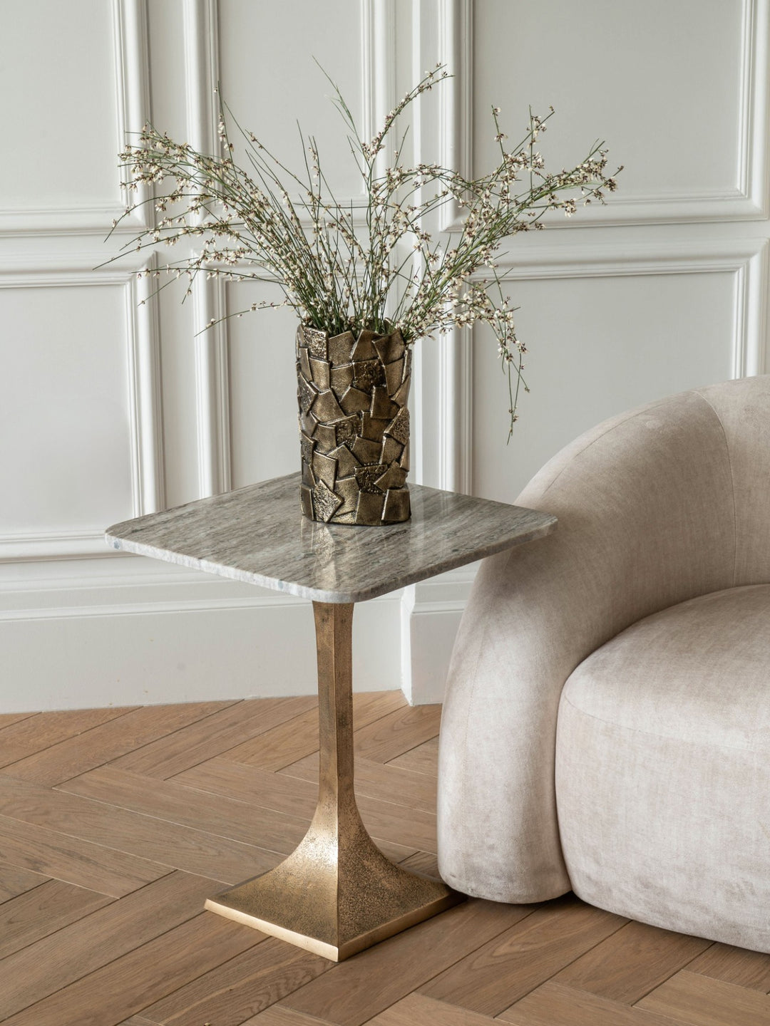Side table with marble top and bronze base next to a beige sofa in a room with panelled walls.