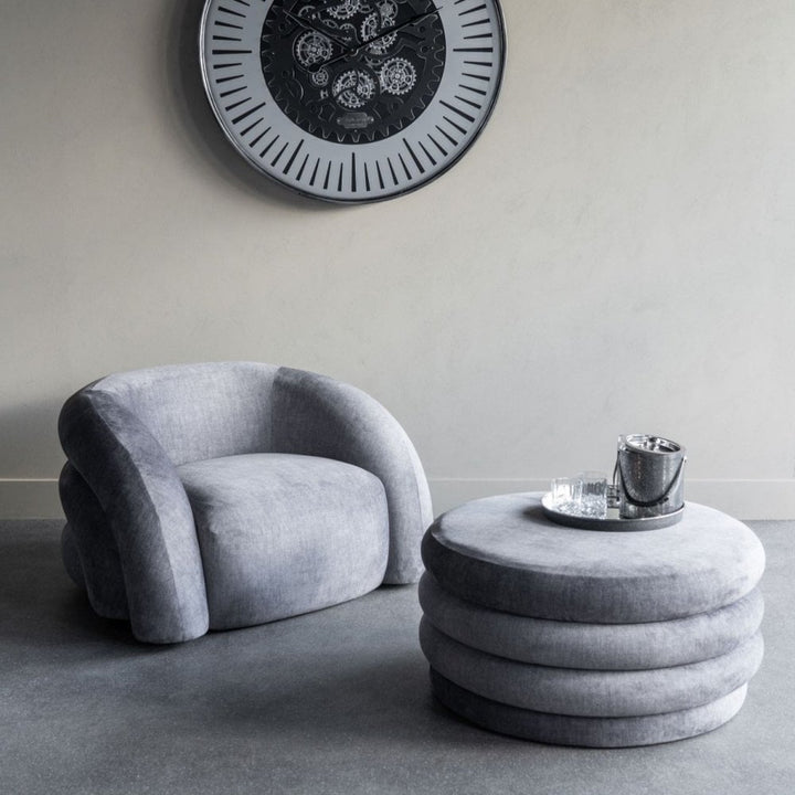 Gray armchair and ottoman with a decorative clock on a light gray wall.