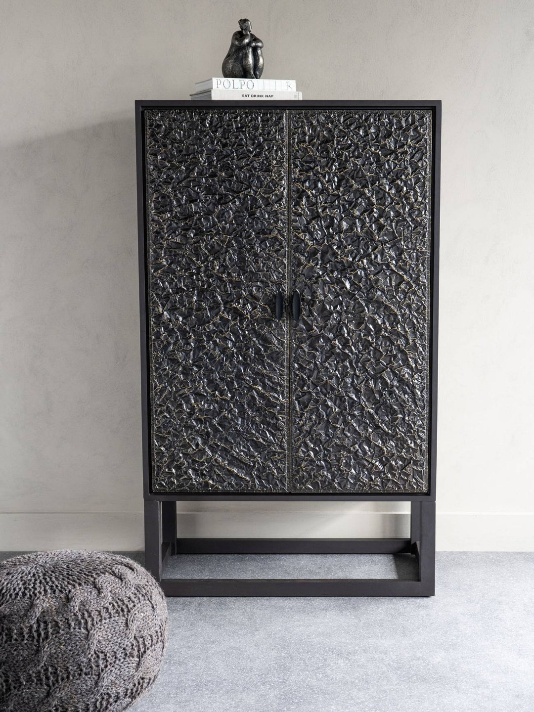 Black textured cabinet with a small statue on top against a plain wall.
