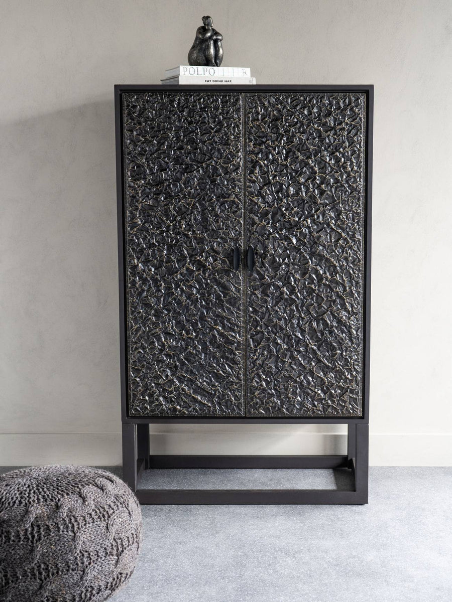 Black textured cabinet with a small statue on top against a plain wall.