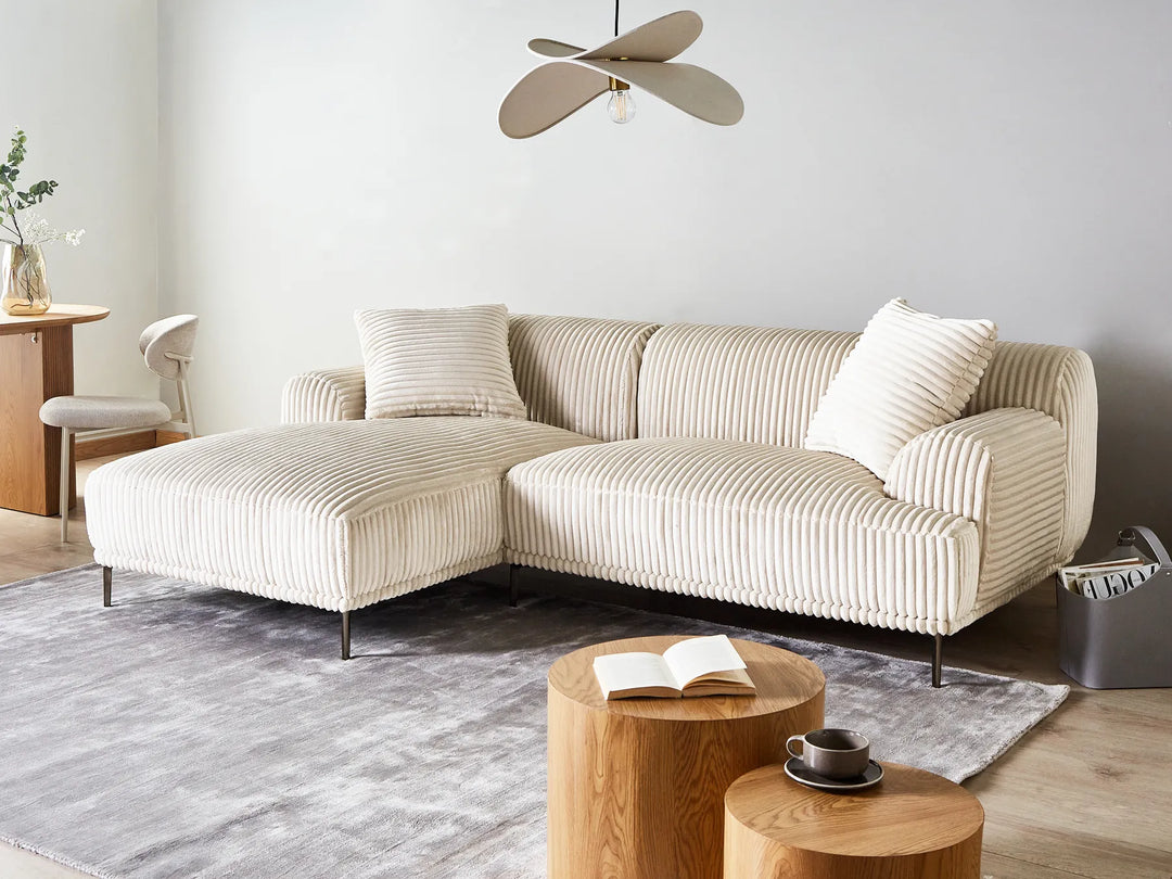 Beige sectional sofa in a living room with wooden coffee table and rug.