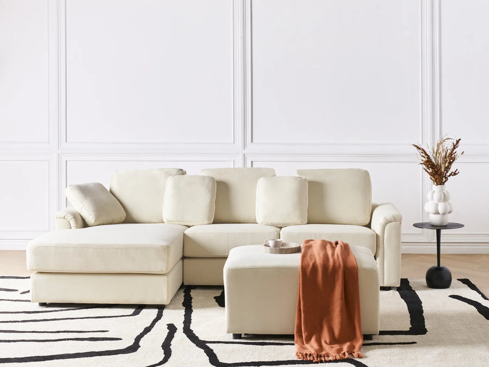 Beige sectional sofa in a living room with a white wall and black and white rug.