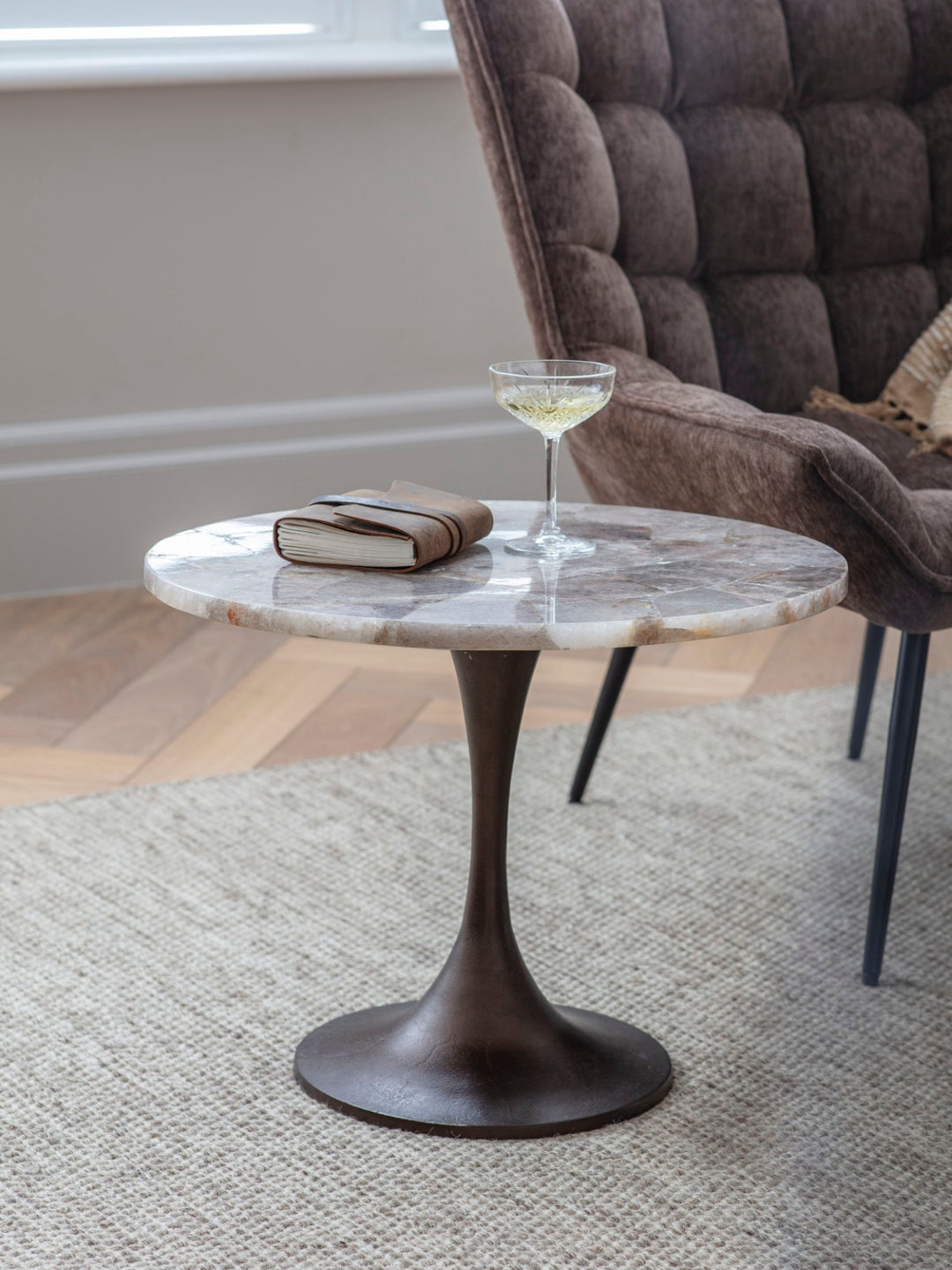 Round marble coffee table with a glass of white wine and a book in a living room setting.