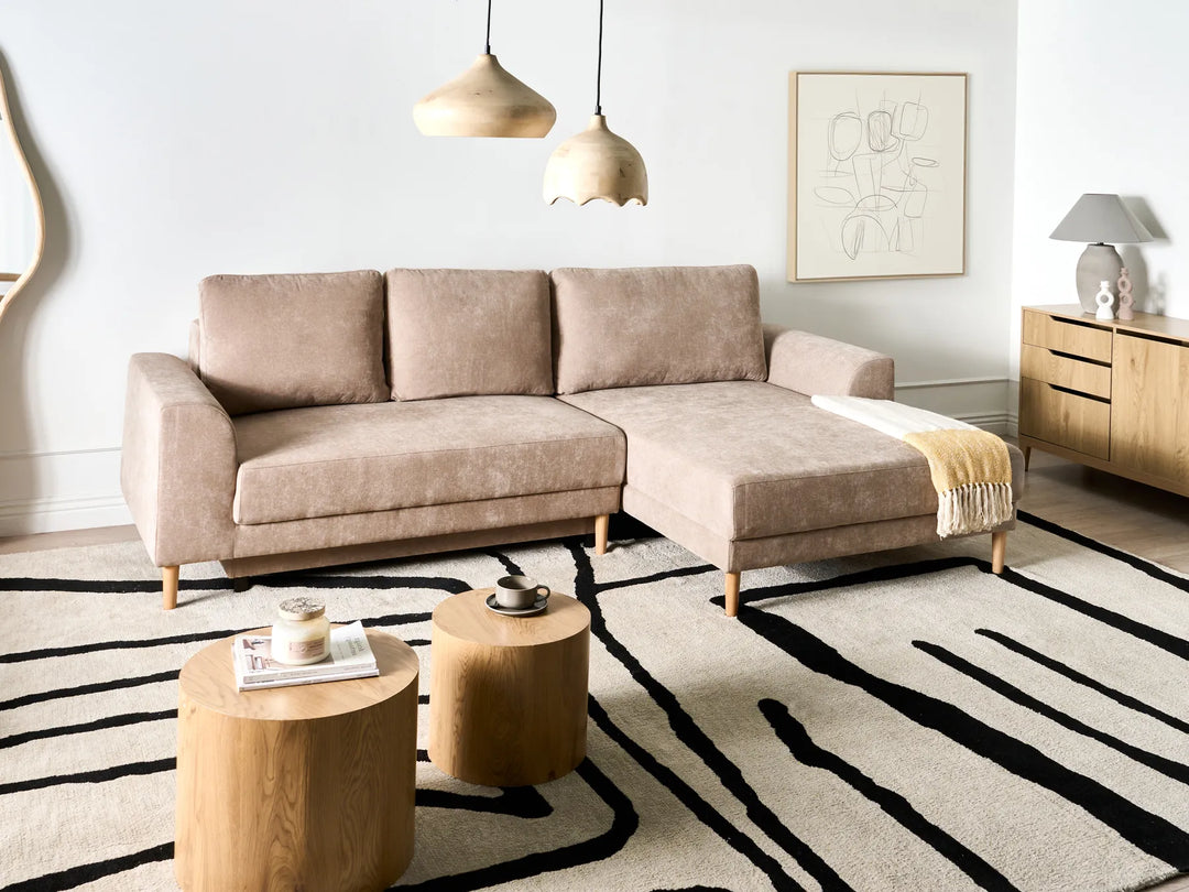 Modern living room with a beige sectional sofa, wooden coffee tables, and a striped rug.