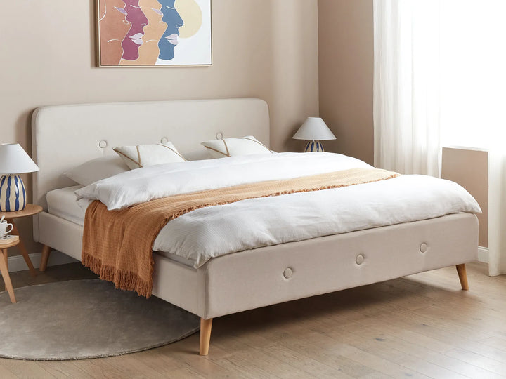 Beige upholstered bed with white bedding and a brown throw blanket in a bedroom setting.