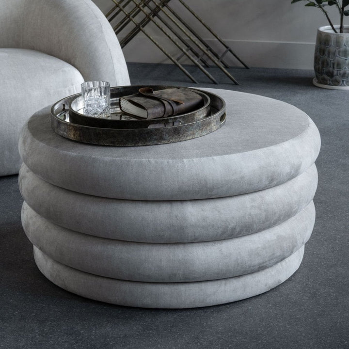 Gray round ottoman with a tray on top in a modern living room setting.