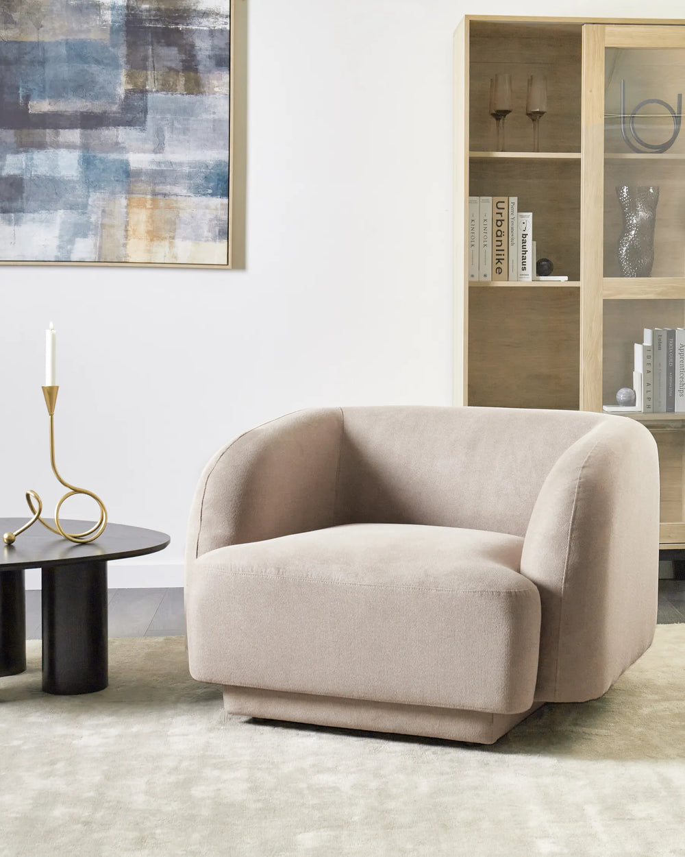 Beige armchair in a modern living room with abstract art and bookshelf.