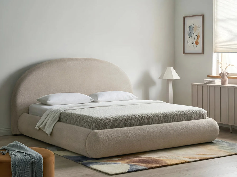 Beige upholstered bed in a modern bedroom setting with a lamp and artwork on the wall.