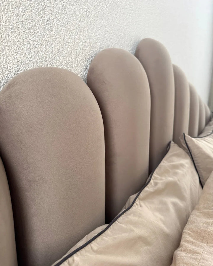 Close-up of a beige upholstered headboard with a textured wall background