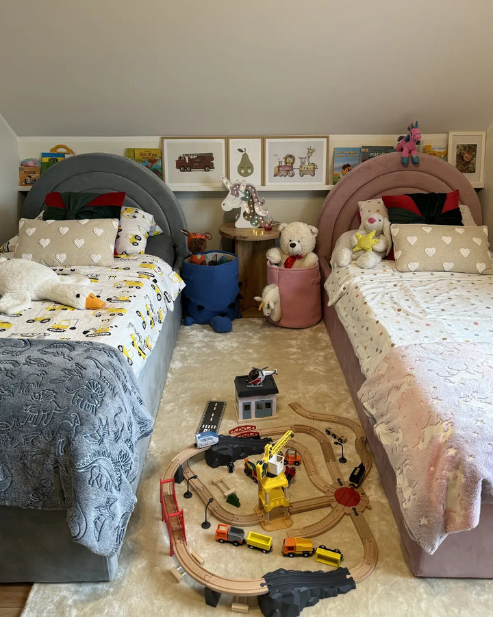 Children's bedroom with two beds, toys, and a toy train set on the floor.