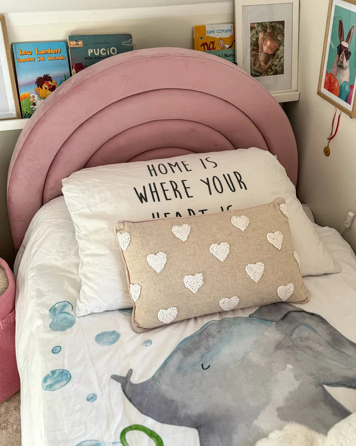 Children's bedroom with pink headboard, decorative pillows, and books on a shelf.
