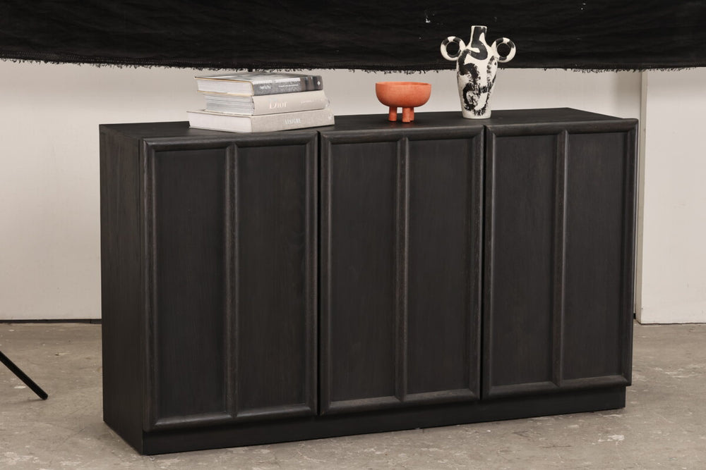 Black cabinet with decorative items on a gray floor and white wall background