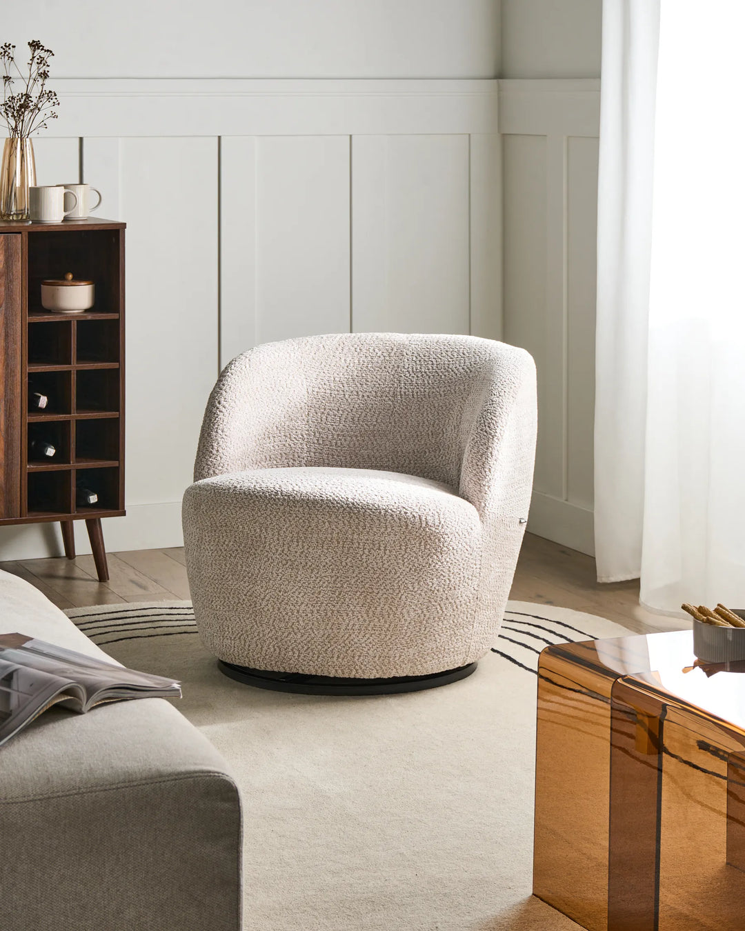 Beige swivel chair in a modern living room setting with a wooden side table and bookshelf.