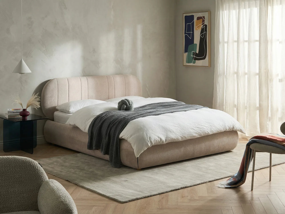 Beige upholstered bed in a modern bedroom with abstract art on the wall.