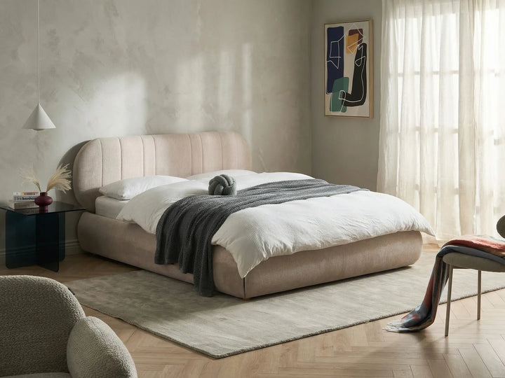 Beige upholstered bed in a modern bedroom with abstract art on the wall.