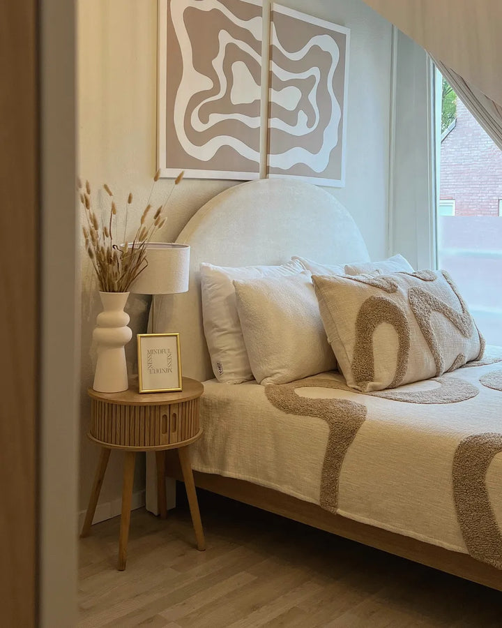 Neatly made bed with decorative pillows and a side table in a bedroom setting.
