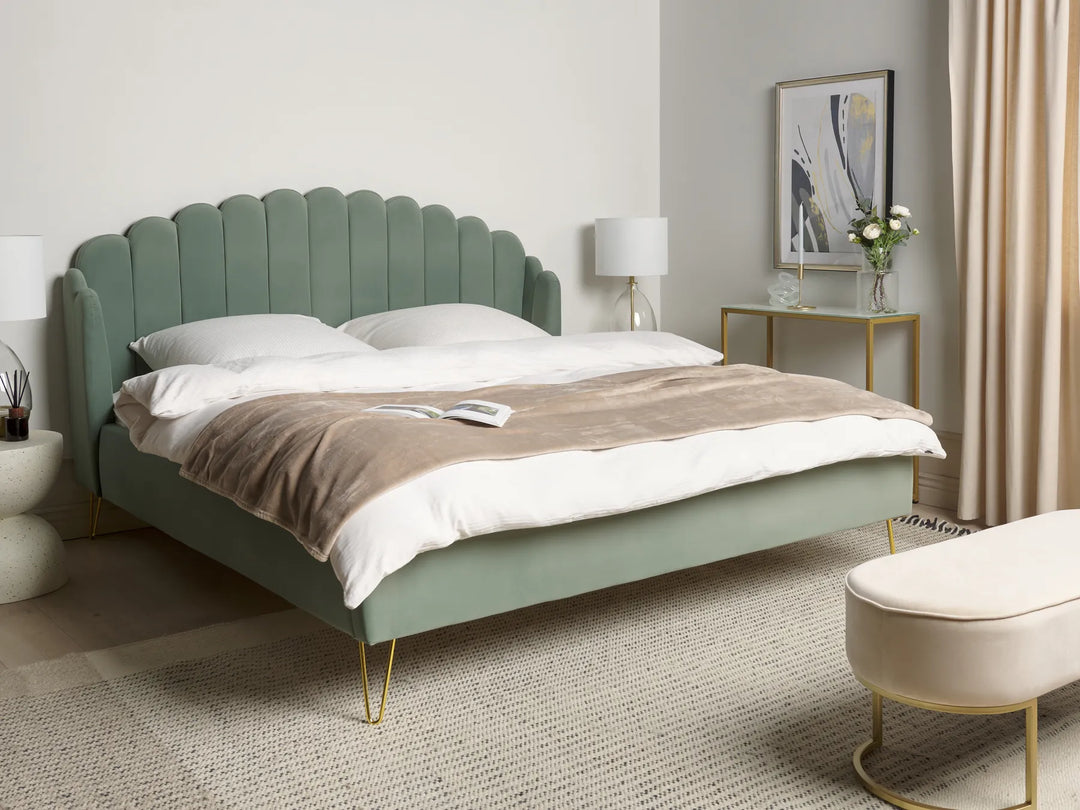 Green upholstered bed in a bedroom setting with a lamp and decor items.