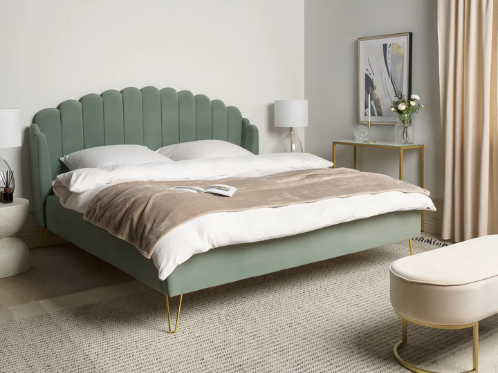 Green upholstered bed in a bedroom setting with a lamp and decor items.