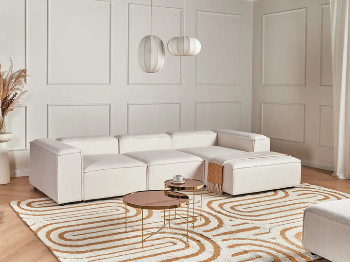 Modern living room with a white sectional sofa, coffee tables, and decorative rug.