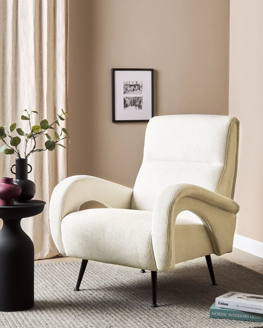 White armchair in a room with a beige wall, framed picture, and decorative items.