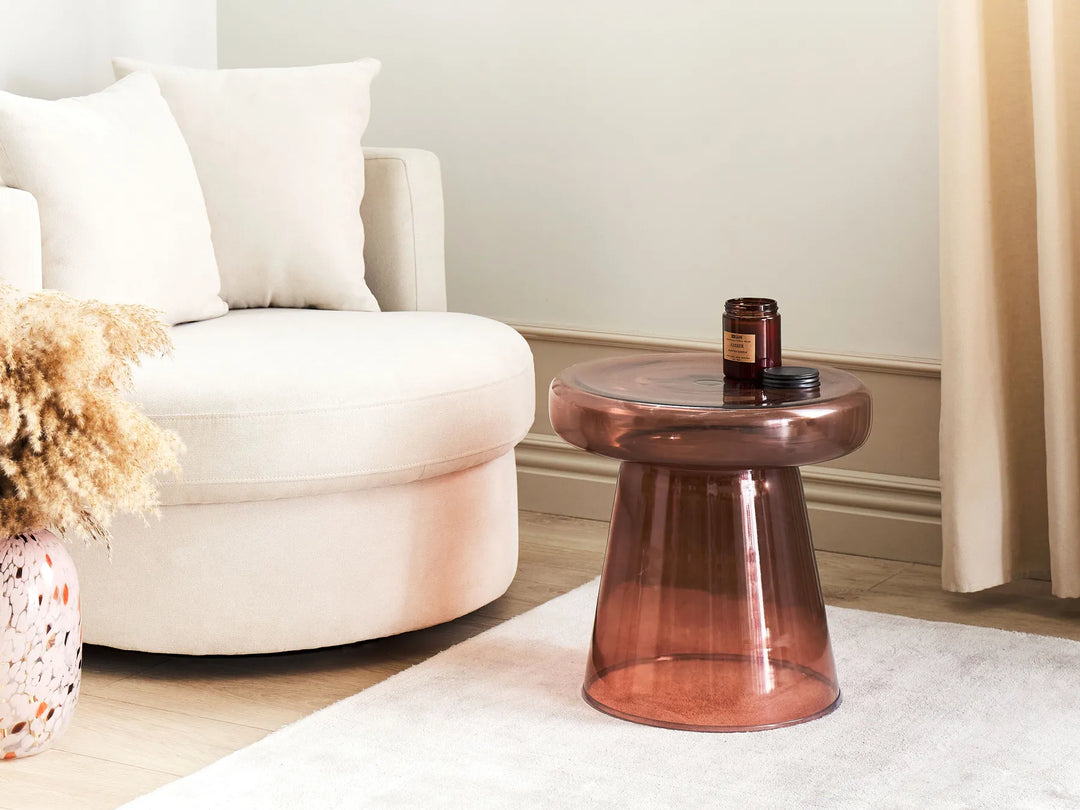 Bronze glass side table in a living room setting with a white armchair and decorative elements.