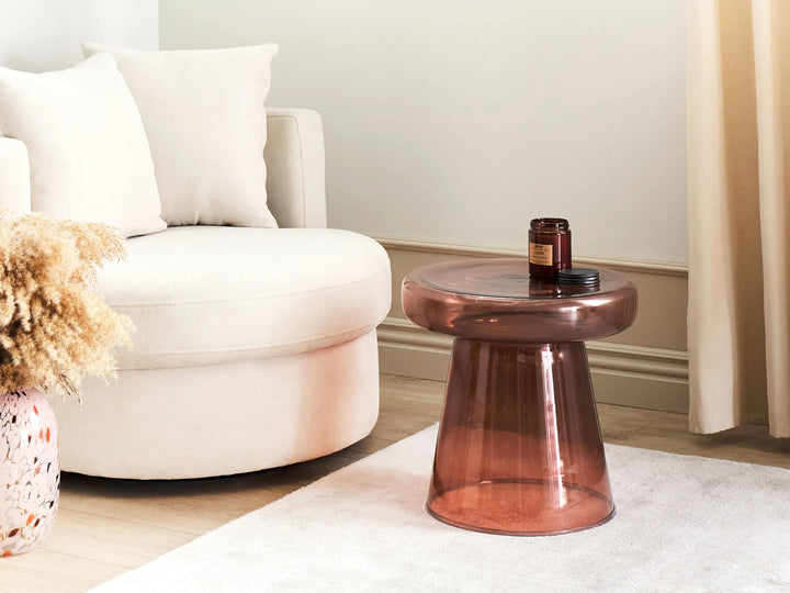 Bronze glass side table in a living room setting with a white armchair and decorative elements.