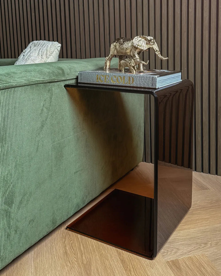 Small black side table with a gold elephant figurine and book against a green sofa and striped wall.